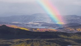 Aerial view of Icelandic highlands with a rainbow over volcanic rock, green moss, geothermal areas, a serene lake, and snow capped mountains. - Powered by Shutterstock - Get 15% off with code: PIKWIZARD15