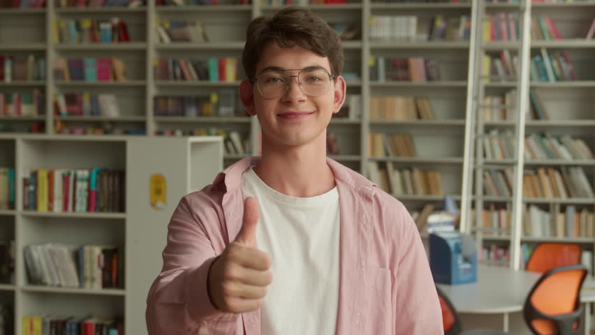Portrait Caucasian teenager guy showing thumb up like gesture good exams result successful study in school college library teen boy happy smiling recommend education studying learning approve hand