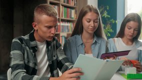 Four teenagers group of classmates Caucasian pupils students together in school doing craft paper art homework reading book instruction girls with boy talking discuss teamwork education in library - Powered by Shutterstock - Get 15% off with code: PIKWIZARD15