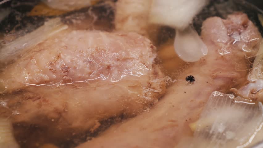 Process of making turkey soup. Boiling broth with turkey legs and vegetables close-up.