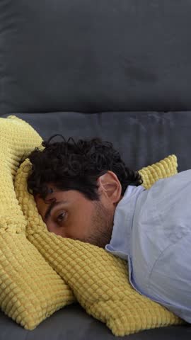 Despair man lying on the sofa and thinking about his problems. Portrait of tired alone serious man having problem in relationship. Unpleasant pain at home interior.