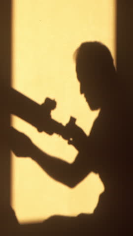 Shadow silhouette of a person sitting in the window and looking through a telescope