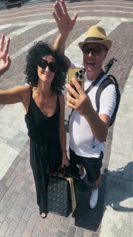 Tourist couple wave hands sending greetings gesture selfie at Dubai reflective hearth sculpture, vertical video, no logos