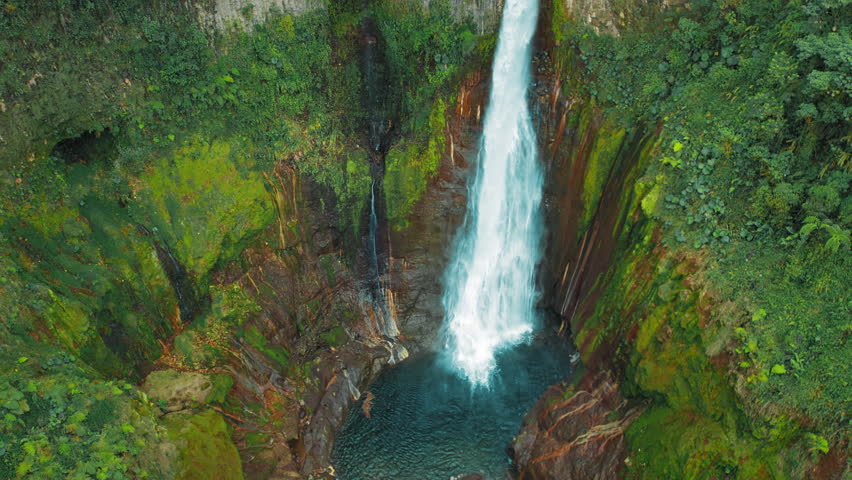Blue Falls waterfall Catarata del Toro crashing into blue basin surrounded by jungle cliffs in Costa Rica