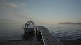 Picturesque view of weathered wooden pier supporting motorboat, gently rocking on mirror-like lake surface during soft early morning light, serene dawn colors reflecting across water, slow motion. - Powered by Shutterstock - Get 15% off with code: PIKWIZARD15