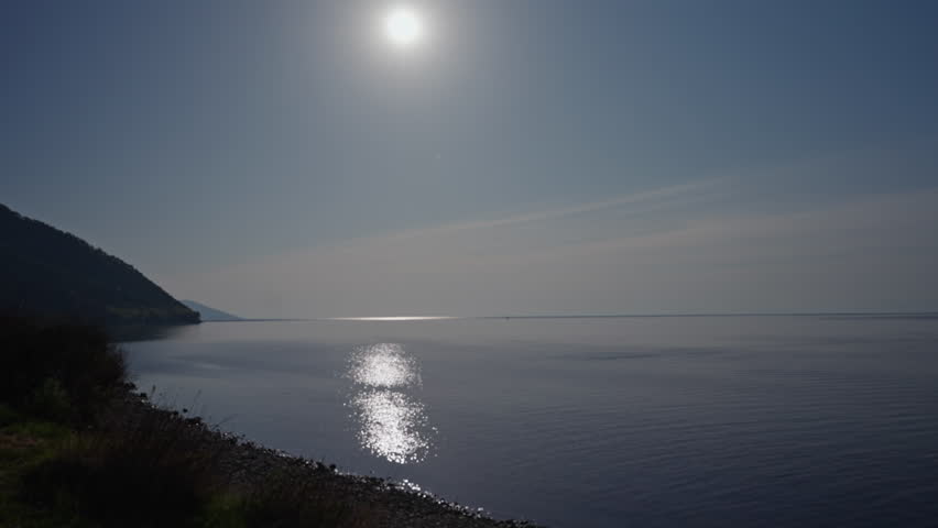 Sun shining over lake Baikal reflecting on water surface with shoreline and hill in background, creating peaceful and scenic landscape in Siberia, Russia, slow motion. Concept of vacation and travel.