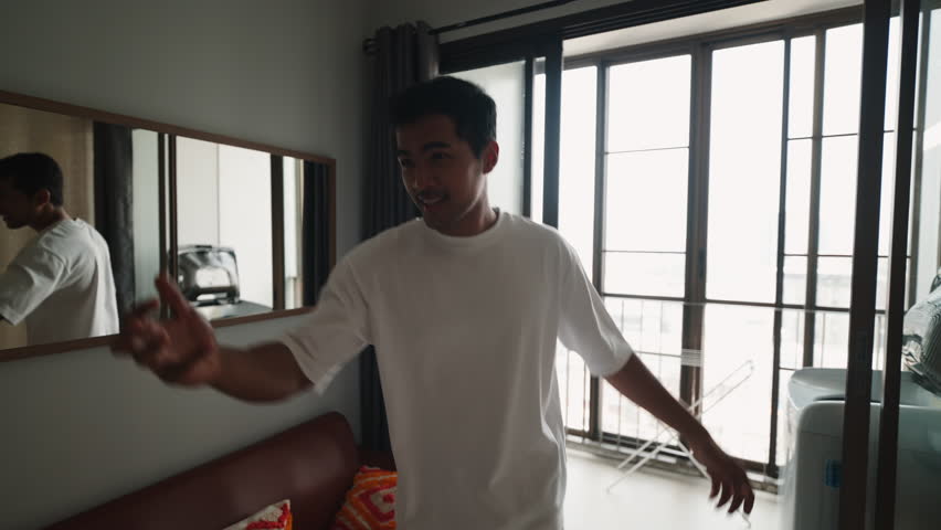 Enthusiastic young burmese man dancing joyfully in his modern apartment