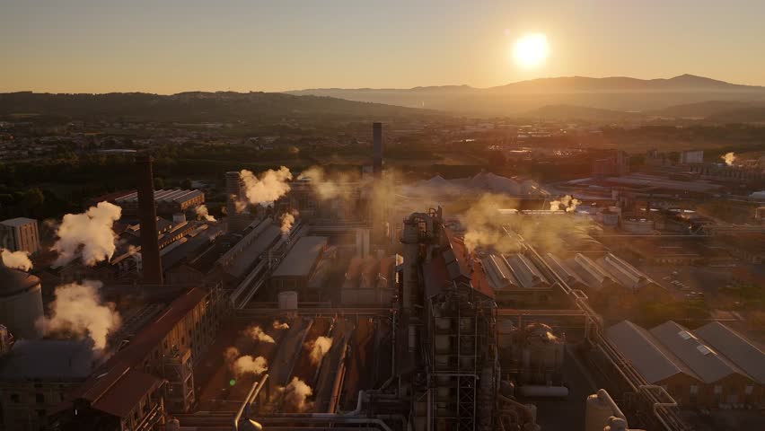 Drone view of vast industrial factory with towering smokestacks, expansive grounds, and glowing sunset sky, highlighting industrial scale and atmospheric evening mood - Powered by Shutterstock - Get 15% off with code: PIKWIZARD15