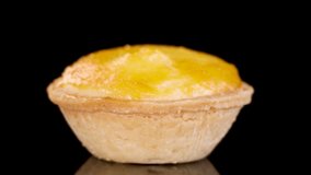 A single egg tart rotates smoothly on a glossy black surface under bright studio lighting, highlighting its golden crust and creamy filling in a controlled environment - Powered by Shutterstock - Get 15% off with code: PIKWIZARD15