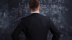 Back View of Man in Formal Suit Standing in Front of Blackboard Filled with Complex Mathematical Equations. Teacher or Scientist Analyzing Formulas and Calculations in Classroom or University Lecture - Powered by Shutterstock - Get 15% off with code: PIKWIZARD15