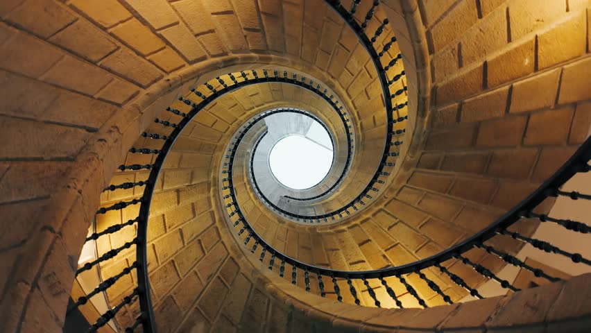 Looking up at a spiral staircase inside a dark building interior. Slow spinning video reveals an abstract architecture background with a hypnotic effect, emphasizing curves, depth and geometric design