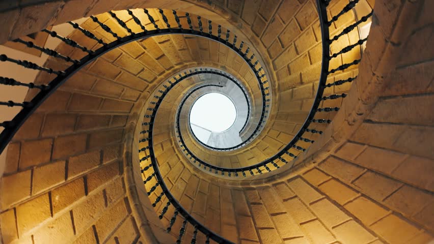 Looking up at a spiral staircase inside a dark building interior. Slow spinning video reveals an abstract architecture background with a hypnotic effect, emphasizing curves, depth and geometric design