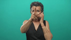 Senior woman with grey hair on phone pointing forward against green background, exuding confidence and engagement. - Powered by Shutterstock - Get 15% off with code: PIKWIZARD15