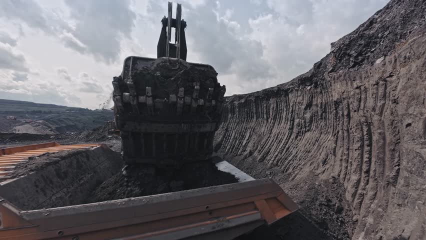 Work of big excavator removes overburden soil to dump truck at open pit mine, FPV drone view of mining industry.