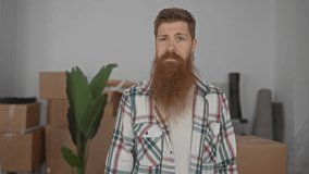 Man with beard holds house key and grins amid stacked moving boxes inside new building foyer; excitement. - Powered by Shutterstock - Get 15% off with code: PIKWIZARD15