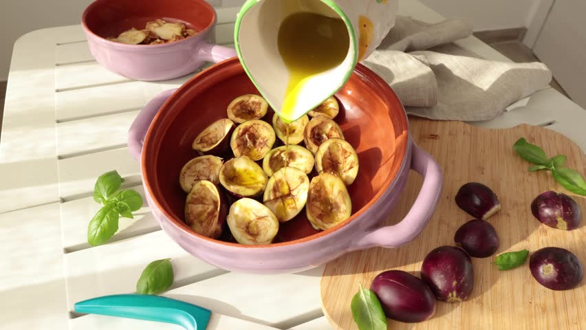 Woman pour olive oil from jug over mini eggplant halves in bowl. Vegetables and healthy eating. Organic produce from the garden.