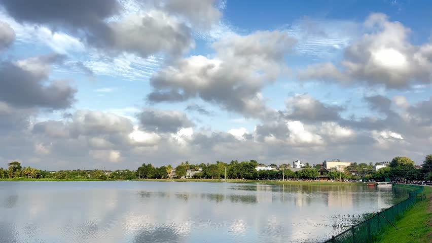 Scenic lake view with dramatic clouds and reflections under a bright blue sky – tranquil nature and urban landscape harmony