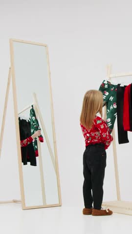 Two children in vibrant holiday sweaters engage playfully in a bright space, reflecting joy and excitement as they interact with a mirror and clothing display