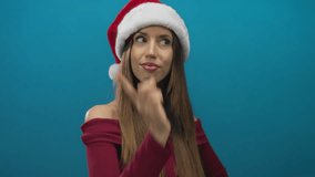 Woman wearing santa hat and red shirt points finger upward while smiling brightly in a blue studio; festive joy. - Powered by Shutterstock - Get 15% off with code: PIKWIZARD15