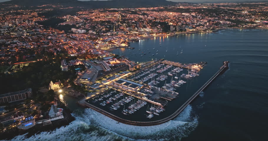 Portugal, Lisbon: Cascais at dusk, breathtaking aerial view showcasing the illuminated night cityscape, marina filled with boats, and the mesmerizing coastline meeting the ocean waves. Drone footage