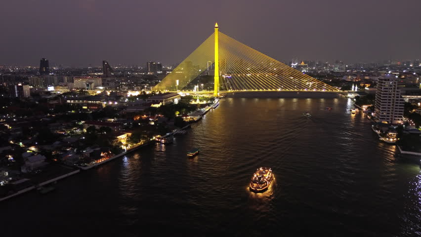 Aerial view of illuminated Rama VIII Bridge at night. Cable-stayed bridge crossing Chao Phraya River in Bangkok, Thailand, 4k