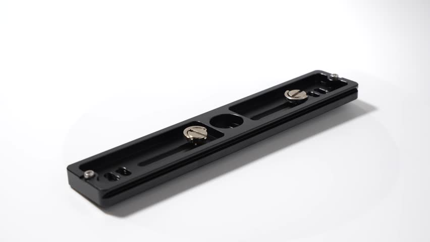 Black aluminum camera quick-release plate shown from the underside with two mounting screws. The white background highlights its shape and details.
