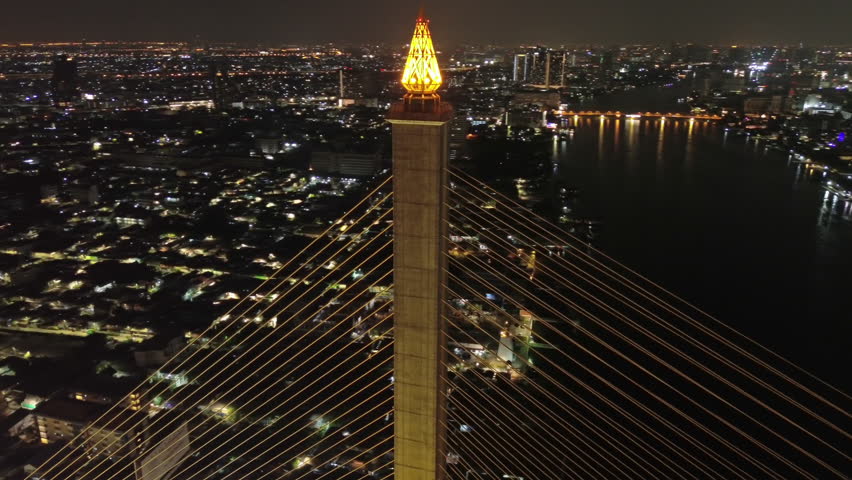 Aerial around view of illuminated Rama VIII Bridge at night. Cable-stayed bridge crossing Chao Phraya River in Bangkok, Thailand, 4k