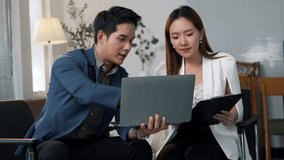Two asian business partners are sitting on chairs in a modern office, collaborating on a project using a laptop, with the man pointing at the screen and the woman holding a clipboard - Powered by Shutterstock - Get 15% off with code: PIKWIZARD15