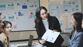 Asian businesswoman leading strategic presentation, guiding colleagues through financial charts and performance data in collaborative modern office environment - Powered by Shutterstock - Get 15% off with code: PIKWIZARD15