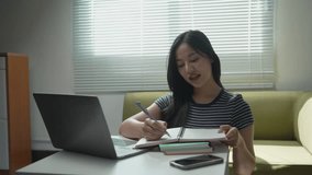 Asian female student carefully taking notes in notebook while studying online, using laptop on white table in bright, sunlit living room interior - Powered by Shutterstock - Get 15% off with code: PIKWIZARD15