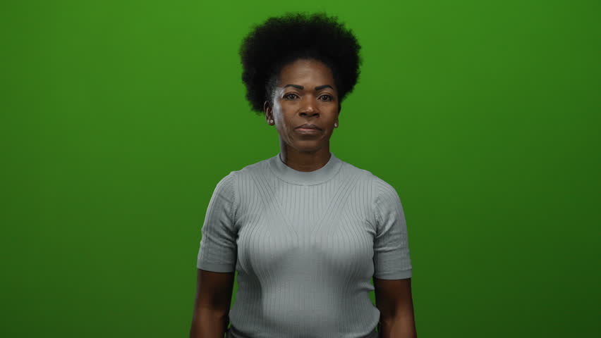 Woman posing confidently against green background with arms crossed embodies strength in minimalist studio setting showcasing focus and power with isolated expression and style.