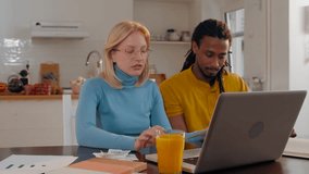 Young multi ethnic couple calculating domestic bills and checking financial status on a laptop in the kitchen - Powered by Shutterstock - Get 15% off with code: PIKWIZARD15