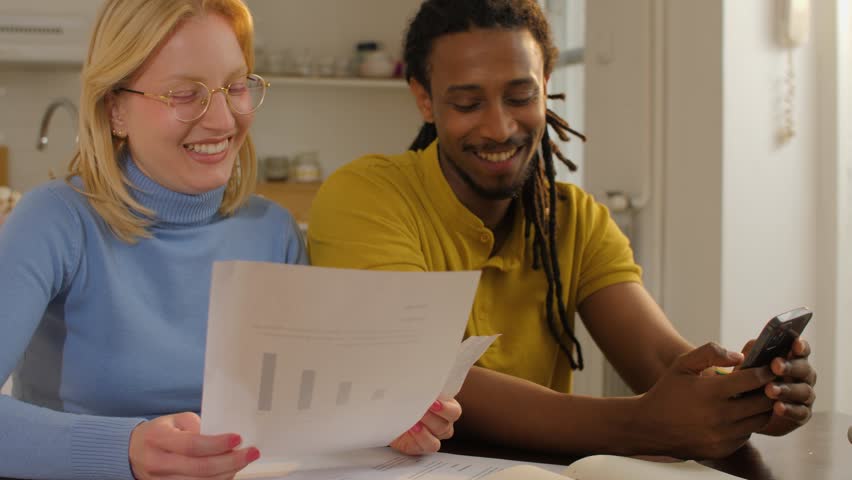 Young multi ethnic couple reviewing financial documents and using smartphone app for online banking and payments