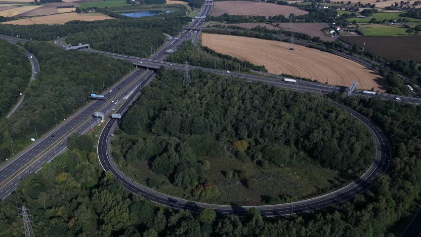 Aerial video of Croft Interchange (Junction 21A) connecting the M6 and M62 motorways near Birchwood, featuring looping slip roads and dense woodland