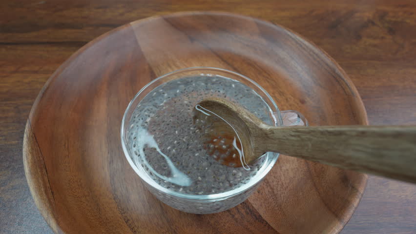 Chia seeds in water. Glass cup with water and chia seeds isolated on wooden plate.