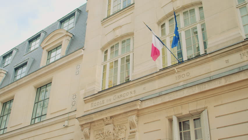 Paris, France -- October 10, 2024. Historic facade of a French boys’ school built in 1900, featuring stone carvings, French and EU flags, and the national motto 
