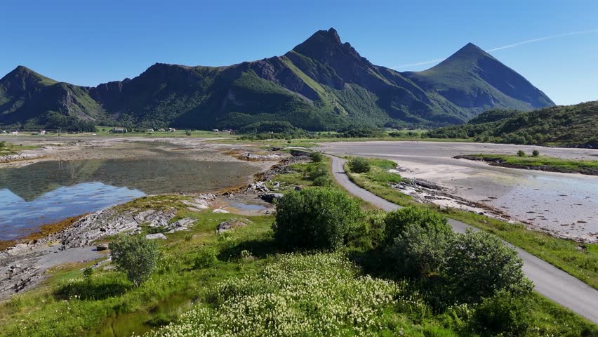 Aerial view of a scenic roadway stretching into the distance on Engeløya in northern Norway, surrounded by tidal sands and dramatic peaks.