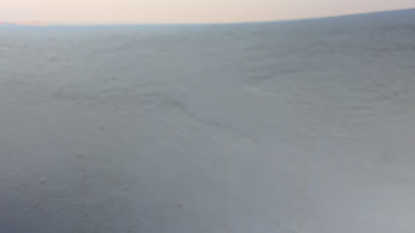 Scenic view of the Santorini caldera from Fira, Greece, filmed with an upward camera movement from a stone wall, showing the blue Aegean Sea with a large ship in the distance.