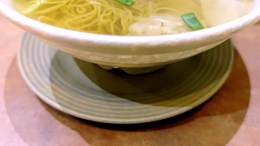 Bowl of freshly cooked steaming hot Wontons (Dumplings) and Egg Noodle Soup. Green vegetables as garnish. Classic Cantonese meal. Catering concept. 4k60.
