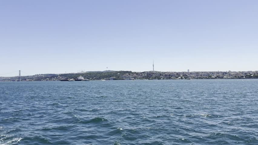 Cinematic view from moving boat gliding on Bosphorus with soft motion of deck, distant Istanbul shoreline, iconic Bosphorus Bridge and passing vessels such as cargo ships, yachts and passenger ferries