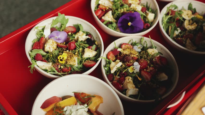 Bright salads in white plates filled with fresh greens, berries, avocado, tomatoes, cucumbers, cheese, chicken and flowers. Restaurant food.
