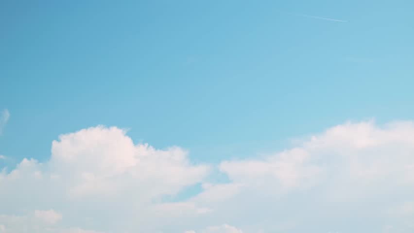 Cumulus clouds floating in the blue sky and an airplane flying high in the sky and contrails. Background material for summer skies. Panning from right to left.