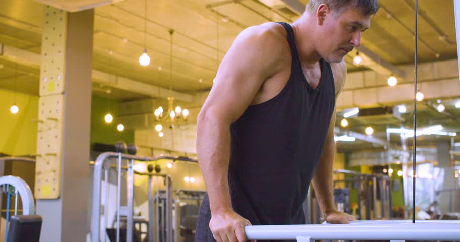 Gym workout. Dips on the bars. Middle aged Caucasian man trains his pectoral and triceps muscles in the gym. Middle-aged man trains pectoral and triceps muscles doing dips on gym bars.