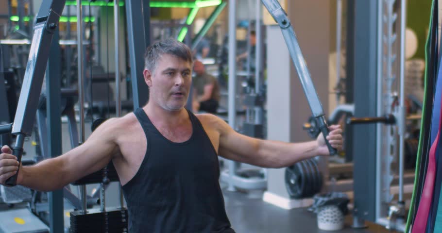 Gym workout. Butterfly exercise. Middle aged Caucasian man trains his pectoral muscles in the gym. Middle-aged man works out chest muscles with butterfly machine at the gym.