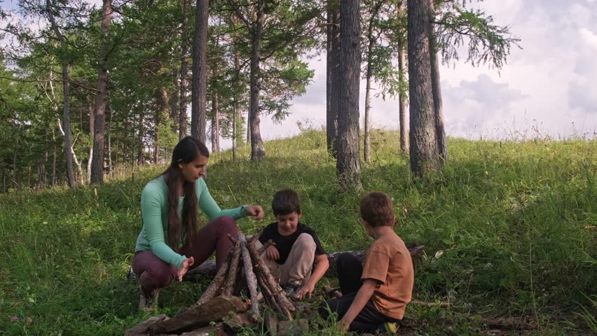 Mother and children building campfire in forest