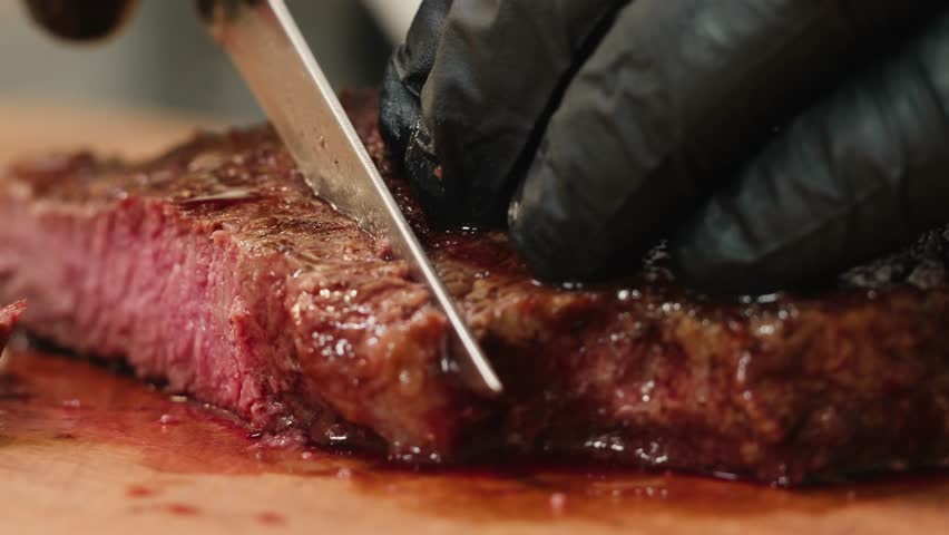 Beef angus steak in restaurant, close up Pieces of hot ribeye steak served on the wooden board. Medium steak slices with blood, salt and pepper in fancy meat cafe. 