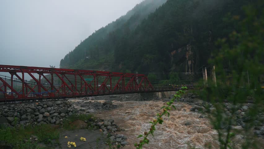4K shot of fast flowing flooded Beas river during rain in mountains at Manali, Himachal Pradesh, India. Vehicle on Metal bridge. Clouds and heavy rain in monsoon season. Flooded river with mud, soil