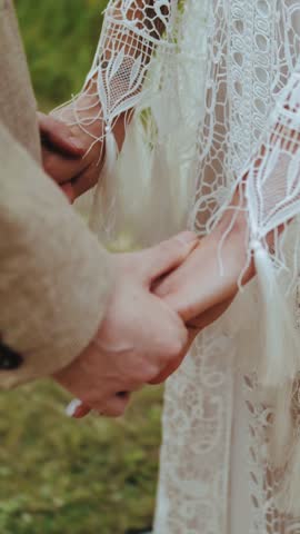 Vertical video. Bride and groom holding hands at a boho wedding ceremony. Touch, love and tenderness. Close-up of a husband and wife holding hands.