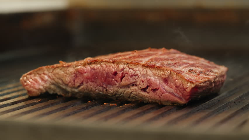 Cooking Beef angus steak in restaurant, close up Pieces of hot ribeye steak served on the wooden board. Medium steak slices with blood, salt and pepper in fancy meat cafe. 