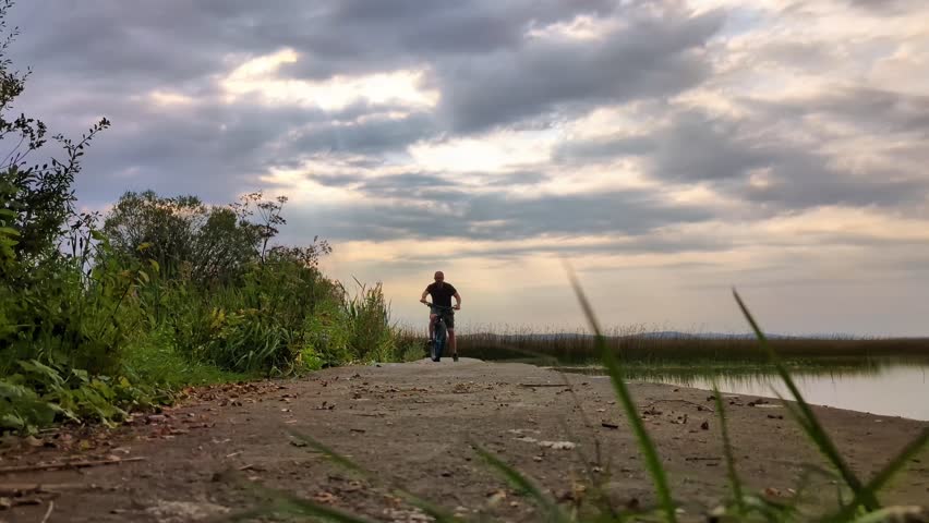 Man Riding Mountain Bike, wheelie on pier Near Lake Under Cloudy Sky, sport and activities, lifestyle, freedom	